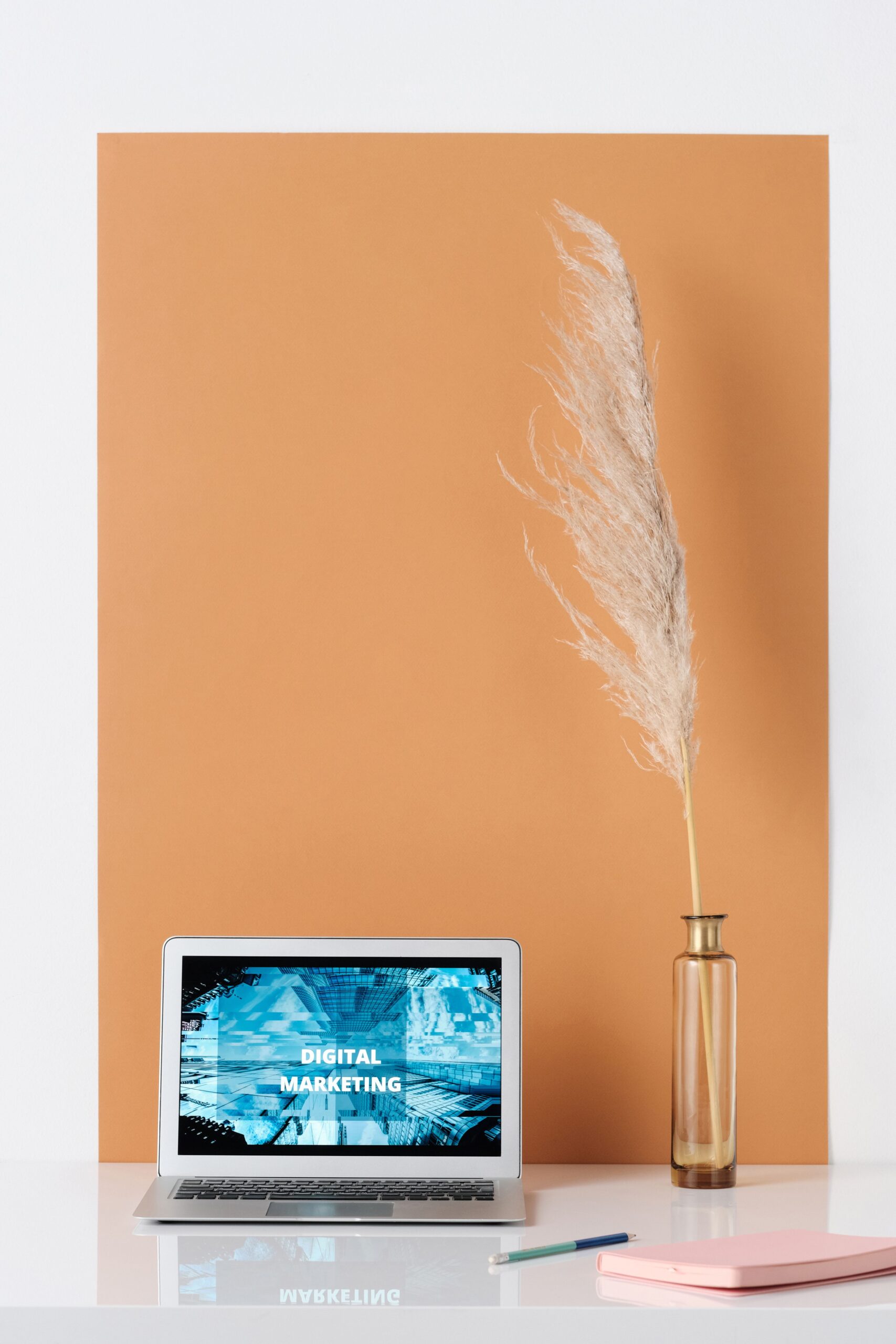 Stylish minimalist workspace with laptop showing digital marketing, vase with pampas grass, and copy space.
